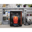 3D printer with orange helmet-shaped object inside.