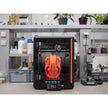 3D printer with orange helmet-shaped object inside.