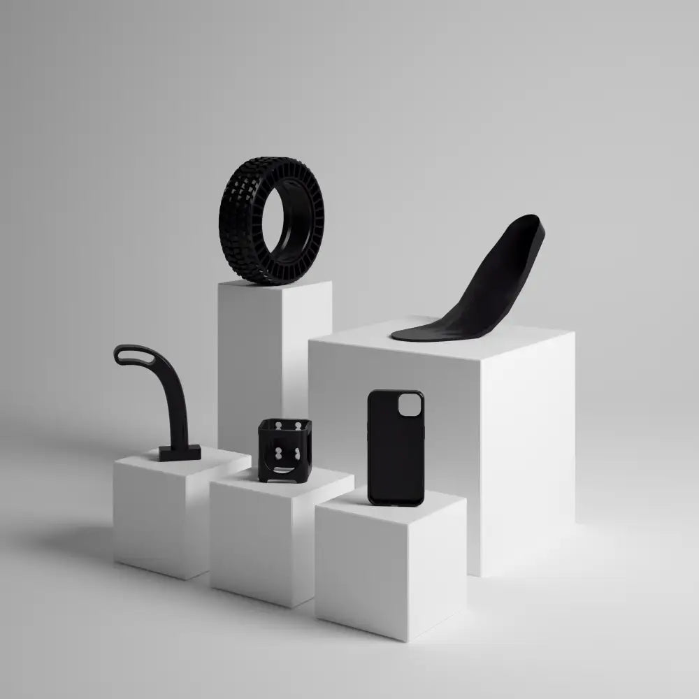 Set of white pedestals displaying various black objects including a tire, seat, phone case, and handlebar.